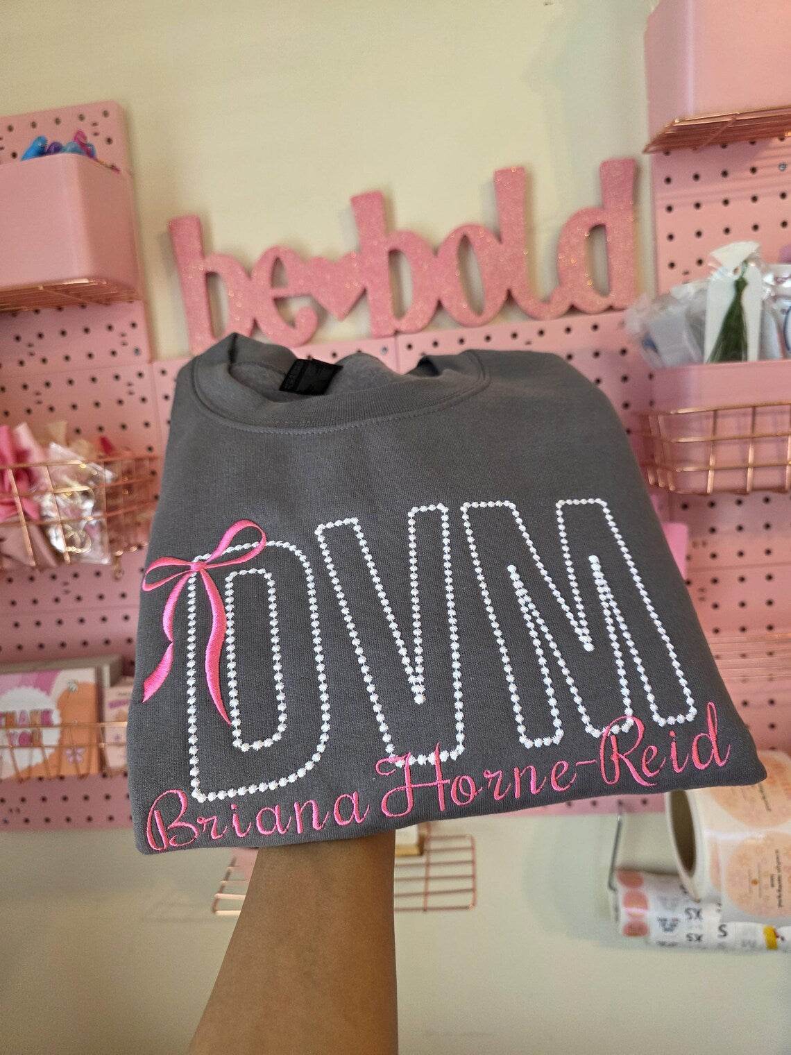 Gray sweatshirt with 'DVM' and personalized text in pink on a pink-themed background.custom-couple-shirt