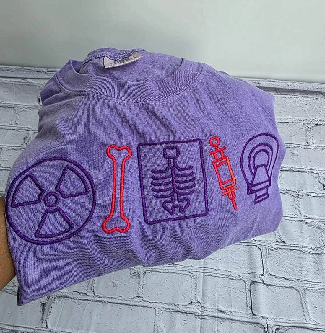 Folded purple t-shirt with medical-themed symbols on a textured surface.radiologist-t-shirt