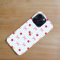 Phone case with cherry and bow pattern on a wooden surface.coquette-phone-case