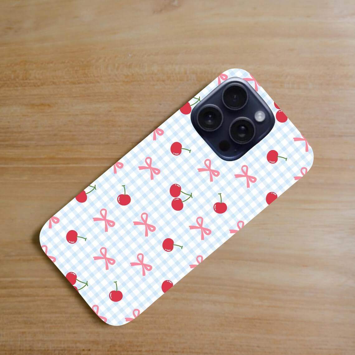 Phone case with cherry and bow pattern on a wooden surface.coquette-phone-case