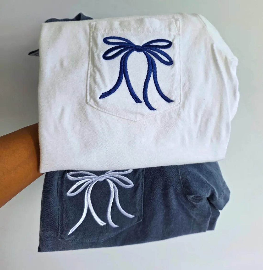 White shirt with blue embroidered bow and navy pants with white embroidered bow on a plain background