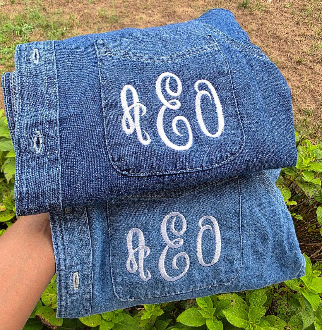 Folded denim jacket with 'AEO' monogram on a green outdoor .custom-bridesmaid-jacketsbackground