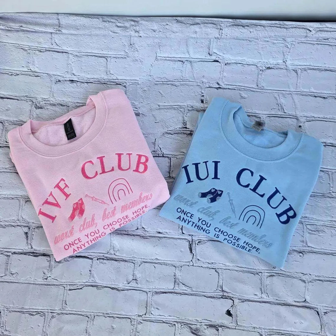 Pink and blue sweatshirts with 'IVE CLUB' and 'IUI CLUB' text on a white brick wall background. ivf-sweatshirt