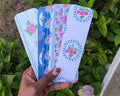 Hand holding four floral-patterned cards against a green leafy background.coquette-floral-bookmarks