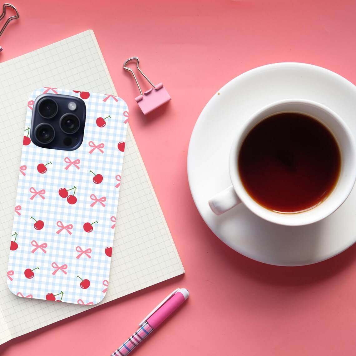 Phone case with cherry pattern on pink surface with coffee cup and stationery.coquette-phone-case