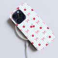 Phone case with cherry and bow pattern on a light gray background.coquette-phone-case
