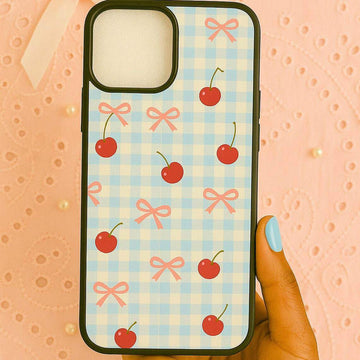 Phone case with cherry and bow pattern held by a hand against a textured pink background.coquette-phone-case