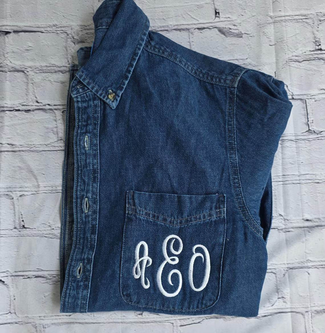 Folded denim jacket with 'AEO' monogram on a green outdoor .custom-bridesmaid-jacketsbackground