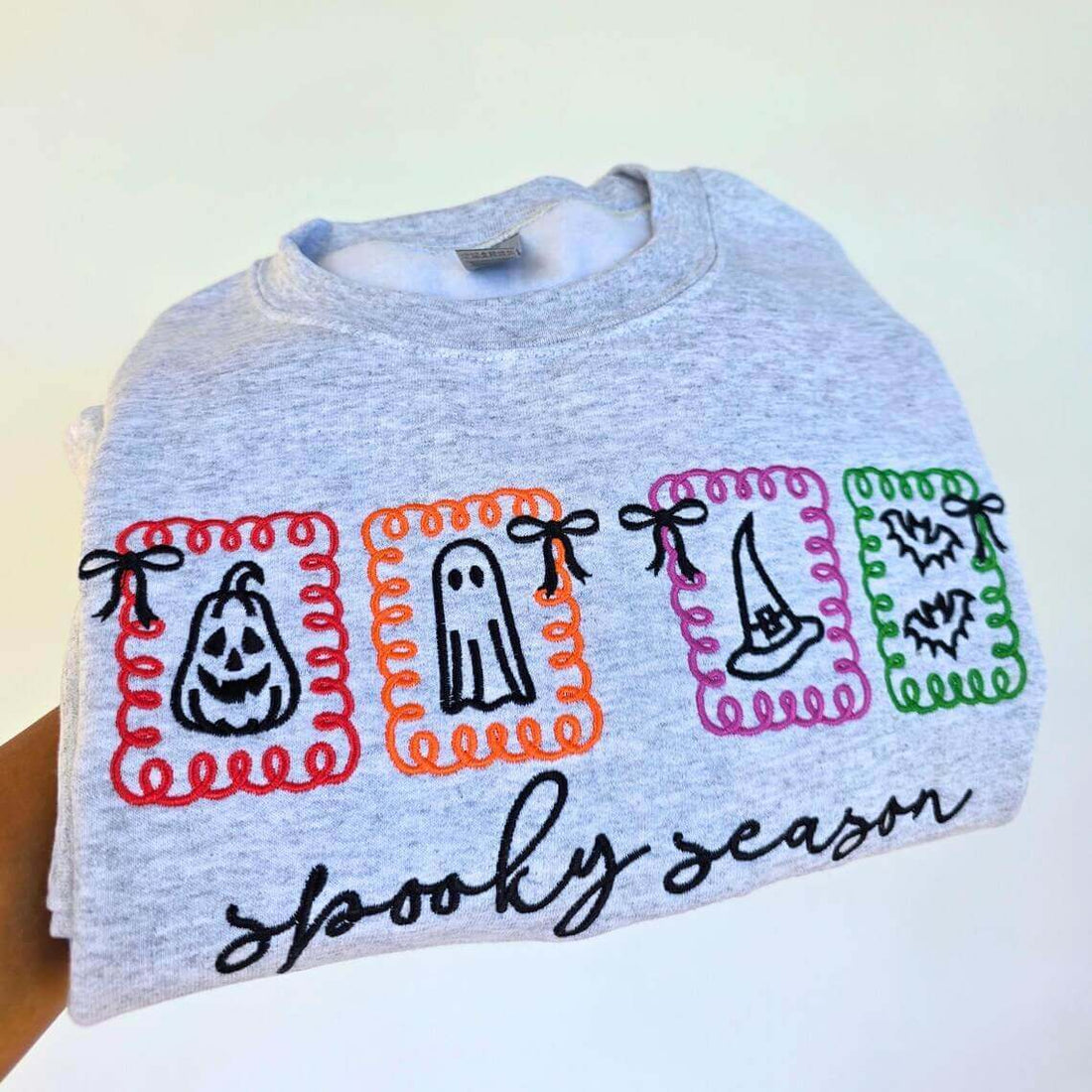 Gray shirt with Halloween-themed designs and text on a white background.halloween-embroidery-sweatshirt