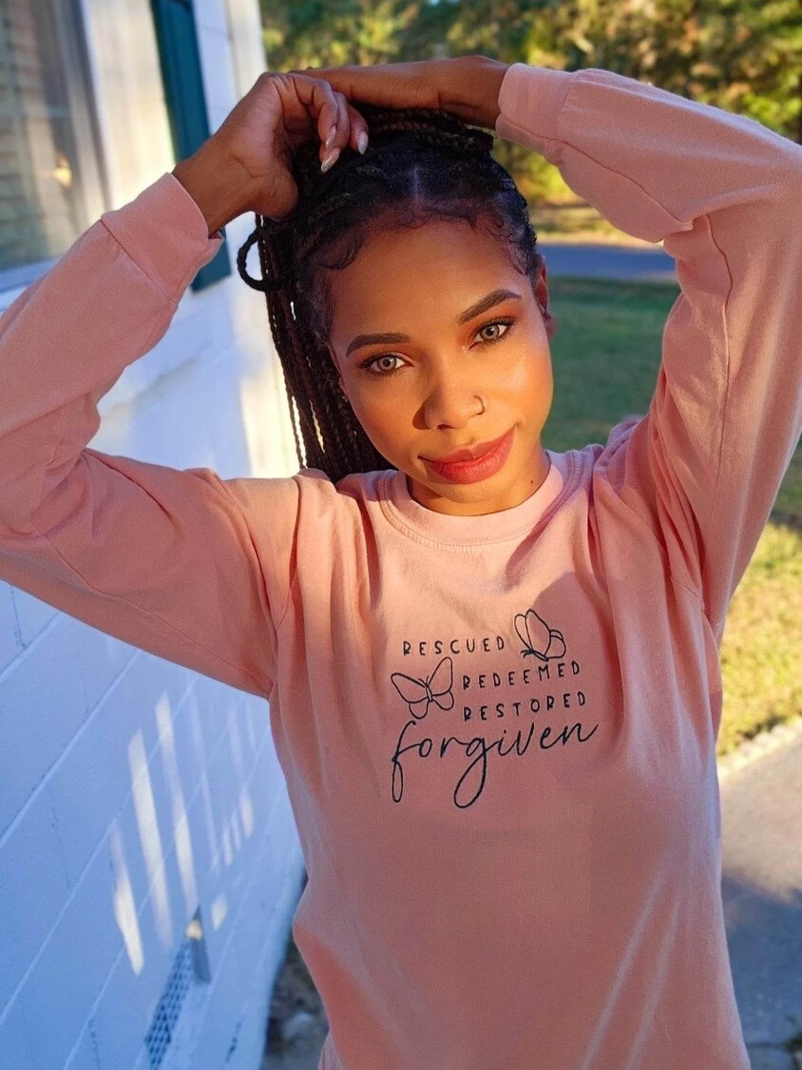 A woman wearing a pink long-sleeve shirt with text and butterfly graphics.forgiven-shirt