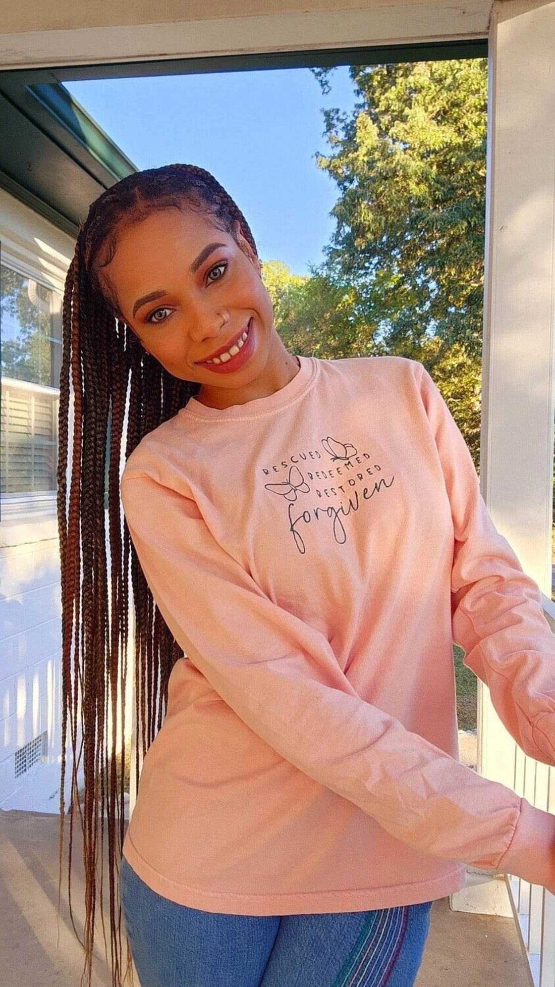 A woman wearing a pink long-sleeve shirt with text and butterfly graphics.forgiven-shirt