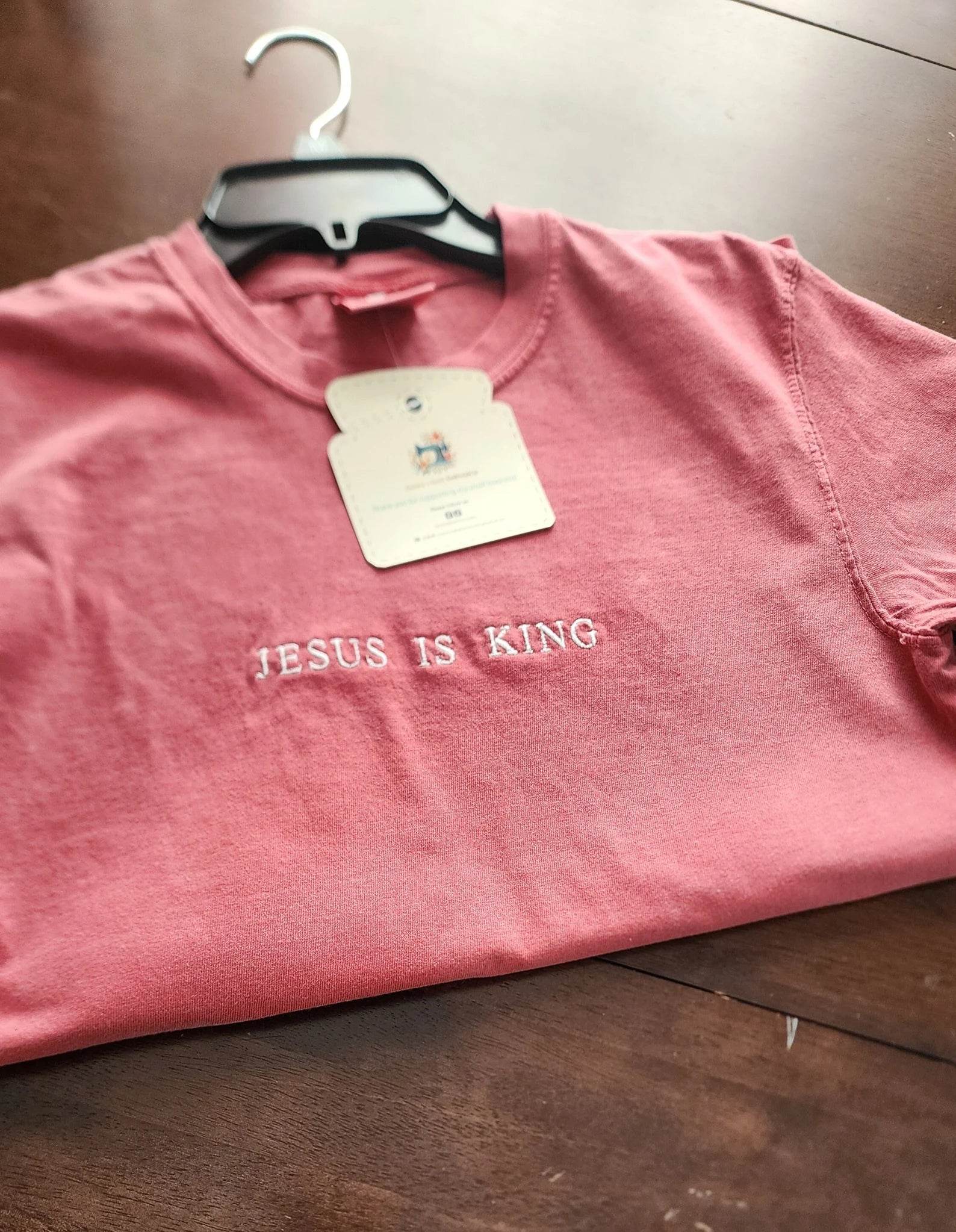 A pink short sleeve shirt with the phrase 'Jesus Is King' embroidered in a darker color across the front.jesus-is-king-shirt