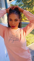 A woman wearing a pink long-sleeve shirt with text and butterfly graphics.forgiven-shirt