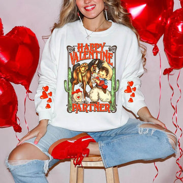 A woman wearing a white crewneck sweatshirt with a 'Happy Valentine Partner' text and graphic design, sitting among red heart-shaped balloons.