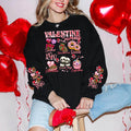 A woman sitting and smiling, wearing a black sweatshirt with a Valentine's Day-themed graphic, surrounded by red heart-shaped balloons.valentines-sweatshirt-for-women