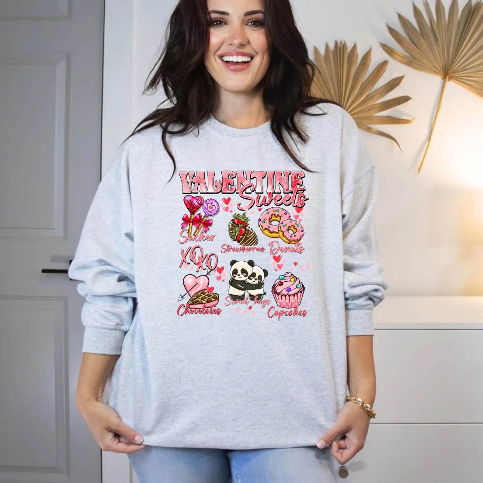 A woman sitting and smiling, wearing a white sweatshirt with a Valentine's Day-themed graphic, surrounded by red heart-shaped balloons.valentines-sweatshirt-for-women